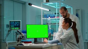 Female research scientist has conversation with man bioengineer next to a desktop computer with green screen mock up. They look at chroma key pc template in a modern science laboratory. video