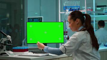 Scientist analysing blood sample and typing at computer with green screen, chroma key display. In background man lab researcher discussing with doctor about vaccine developent. video