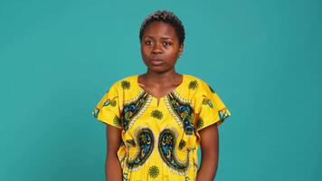 Young adult feeling uncertain and raising shoulders in studio, being unsure and indecisive against blue background. Doubtful clueless girl acting confused about something unknown. Camera A. video