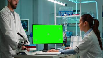 Biochemistry scientists developing drugs, female microbiologist doing research working on computer with green screen chroma key display. In background man lab researcher bringing blood samples video