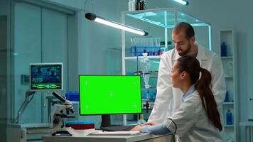 profissional químicos trabalhando em computador com verde tela zombar acima e teste vírus evolução, em desenvolvimento vacina, drogas e antibióticos. em pé dentro Alto tecnologia laboratório com croma chave exibição video