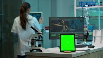 team av vetenskapsmän arbetssätt i bakgrund av modern laboratorium använder sig av läsplatta med grön skärm, attrapp visa, isolerat krom nyckel övervaka, analyserar experimentera Evolution, hög tech utveckling labb. video