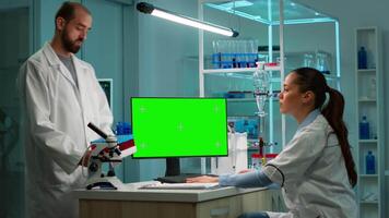 Microbiologist working on computer with display, green chroma key screen talking with coworker about new vacutainer with blood samples. Team of biotechnology scientists developing drugs. video
