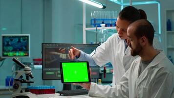 Professional chemists working on tablet with green screen mock up and testing virus evolution, developing vaccine, drugs and antibiotics standing in high tech laboratory with chroma key display video