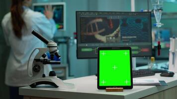 forskare stående på övervaka i bakgrund analyserar virus Evolution medan läsplatta med mock-up grön skärm arbetssätt i främre. man labb forskare granskning vaccin utvecklande föra blod prover video