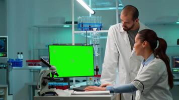 Modern medical research laboratory with two scientists using computer with green chroma key screen. Doctors specialists discussing innovative treatment, advanced scientific lab for medicine. video