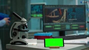 mikrobiolog föra blod prover i modern labb sätta dem nära smartphone arbetssätt med grön krom nyckel skärm placerad på skrivbord. team av bioteknik vetenskapsmän utvecklande läkemedel i bakgrund video