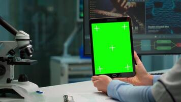 Close up of scientist woman holding tablet with green mockup in modern equipped lab. Team of microbiologists doing vaccine research writing on device with chroma key, isolated display. video
