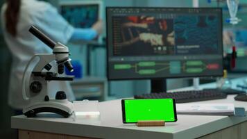 Horizontal mobile phone with green screen working in labooratory with mock up template, chroma key display while professional engineer testing virus evolution in background. High tech development lab. video