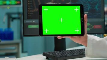 Close up of scientist man holding tablet with green mockup in modern equipped lab. Team of microbiologists doing vaccine research writing on device with chroma key, isolated display. video