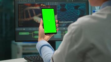 tillbaka se av mikrobiolog läkare kvinna ser på mobil telefon med grön attrapp i modern utrustad labb. team av forskare håller på med vaccin forskning skrivning på enhet med krom nyckel, isolerat visa video