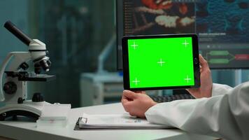 Back view of chemist man holding tablet with green mockup in modern equipped lab. Team of microbiologists doing vaccine research writing on device with chroma key, isolated display. video