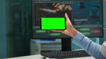 Close up of scientist woman holding smartphone with green mockup in modern equipped lab. Team of microbiologists doing vaccine research writing on device with chroma key, isolated display. video