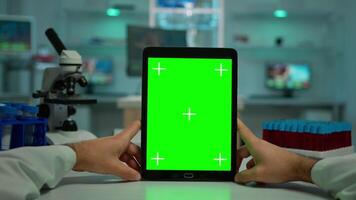 POV shot of chemist using tablet with green screen in biological laboratory. Medical worker wearing white coat in clinic working with notebook with chroma key on isolated display in medical lab video