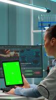 Vertical . Microbiologist working on notepad with green chroma key display in modern equipped lab. Team of biotechnology scientists developing drugs using tablet with mock up screen. video