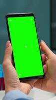 Vertical . Close up of doctor's hand holding phone with green screen sitting at desk in biological laboratory while nurse bringing blood samples. Scientist using smartphone with mockup, chroma key display video