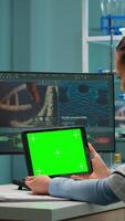 Vertical . Scientist holding tablet with green mockup, looking on device with chroma key, isolated display. Microbiologists doing virus research, in background man lab researcher working at vaccine developent. video