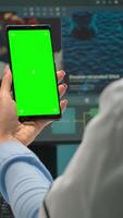 Vertical . Back view of microbiologist doctor woman looking at mobile phone with green mockup in modern equipped lab. Team of scientist doing vaccine research writing on device with chroma key, isolated display video