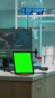Vertical . Microbiologist working on monitor in background analysing test samples with tablet with green chroma key screen placed on desk in front. Team of biotechnology scientists developing drugs. video