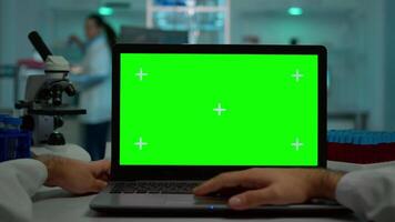 pOV skott av mikrobiolog skriver på bärbar dator med grön krom nyckel visa Sammanträde på skrivbord arbetssätt läsning virus symtom. i bakgrund labb forskare analyserar vaccin utvecklande granskning prover video