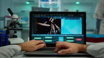 pov Disparo de bioquímico analizando vacuna evolución en ordenador portátil sentado a escritorio laboral, examinando virus síntomas. en antecedentes laboratorio investigador comprobación y preparando químico utensilios video