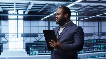 Software engineer in data center runs error checking utilities on tablet to fix problems. IT specialist looking for network issues affecting rigs performance using digital device, camera A video