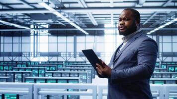 IT operator doing maintenance using tablet to prolong data center equipment life span. IT professional in server hub workspace monitoring server mainframes using digital device, camera B video