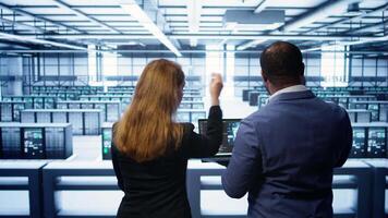 Teamworking programmers in data center overseeing server operations using laptop and tablet. Coworkers ensuring optimal performance and data integrity in server room using devices, camera B video