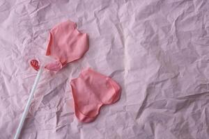 A burst pink balloon heart on a stick lies on a background of pink crumpled paper. A place for your text photo