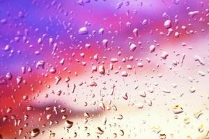 Rain drops on the window glass against the background of bright colored sunset clouds photo