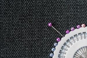 Fragment of a white sewing needles container on a dark textured fabric surface. Top or flat view with copy space photo