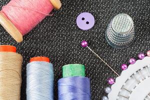 Sewing accessories spools of threads, needles, thimble, button on the textured fabric surface photo