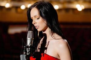 A luxurious actress in a red dress sings on stage with a microphone in her hands photo