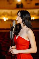 A luxurious actress in a red dress sings on stage with a microphone in her hands photo
