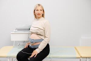 Woman pregnant checking fetal heart beat by fetal monitoring. Expectant mother with midwife adjusting sensors off cardiotocography photo