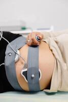 Woman pregnant checking fetal heart beat by fetal monitoring. Expectant mother with midwife adjusting sensors off cardiotocography photo