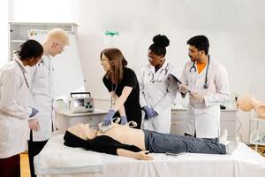 A group of five medical students stand around a training dummy, practicing CPR in a medical training facility photo