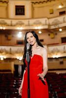 A luxurious actress in a red dress sings on stage with a microphone in her hands photo
