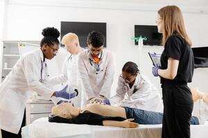 A group of five medical students stand around a training dummy, practicing CPR in a medical training facility photo