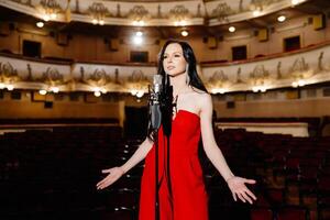 A luxurious actress in a red dress sings on stage with a microphone in her hands photo