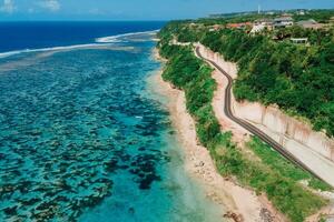 Beach under cliff with road. Coastline and turquoise ocean in Bali island. Aerial view photo