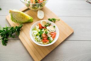 fresh vegetable salad, cabbage, tomatoes in a bowl on a wooden table photo