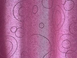 A pink fabric with a subtle sheen, decorated with an abstract pattern of black circles and ovals, creating a modern and elegant look. photo