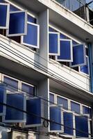 A building facade with multiple blue-tinted windows, some of which are open, creating a visually striking pattern. photo