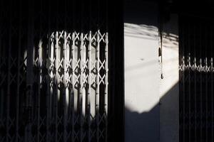 A metal security gate with a lattice design, partially illuminated by sunlight. photo