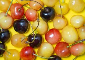Sweet cherry with a stem on a yellow background. Bright table. Berries on the table. Delicious food. Berries of different colors. photo