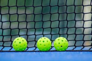 tree green pickleball balls next to the net of a pickleball court photo