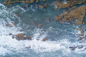 foam of the waves on the shore of a rocky coast, aerial overhead view with drone photo