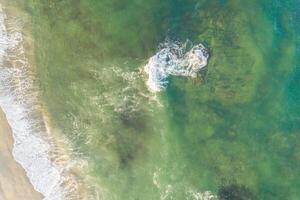 aerial directly above drone view of a beach with turquoise water and a rock near the shore photo