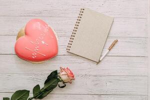 Heart shaped pink mousse cake on table with rose and notepad. photo